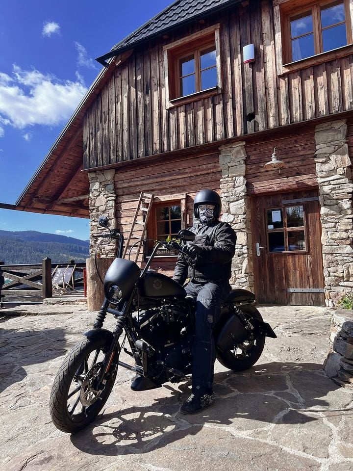 Motorkář na motorce před roubenkou penzionu