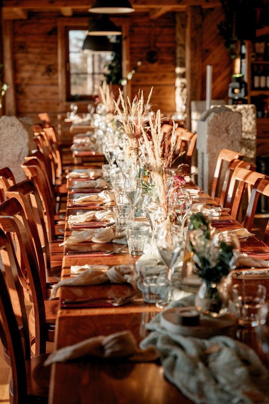 Dlouhá svatební tabule v dřevěné restauraci, sušené trávy, svíčky a lněné ubrousky
